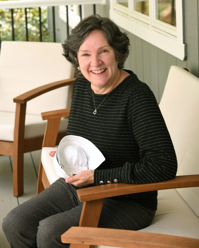 Cynthia Willis is seated, holding her nursing cap.
