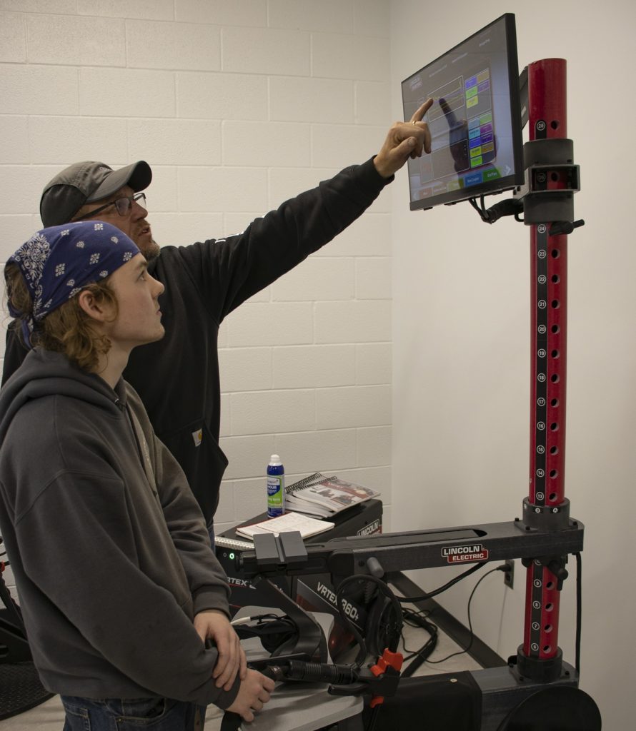 Virginia Western faculty member Gary Young reviews results on the VRTEX virtual reality welding simulator with Josh Simmons, who used the machine to practice stick welding.
