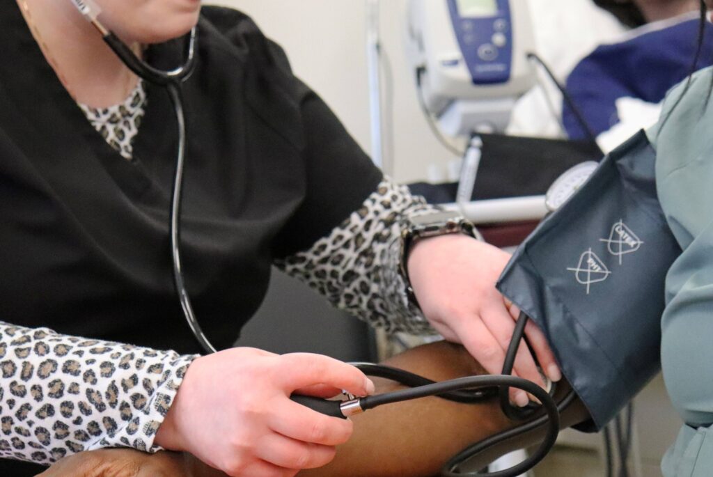 A person is seated taking the blood pressure of another seated person.