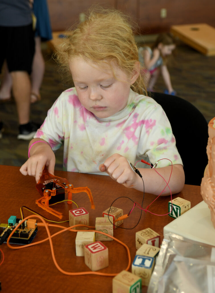 Aurora Garrett, 6, is using muscle activity to control a robot at STEM Day at Virginia Western Community College. The Roanoke-Blacksburg Innovation Alliance exhibit let students experience the kind of technology developed at RBIA's Innovation Studio. RBIA supports the Roanoke region's life sciences startups with a focus on medical devices and digital health.