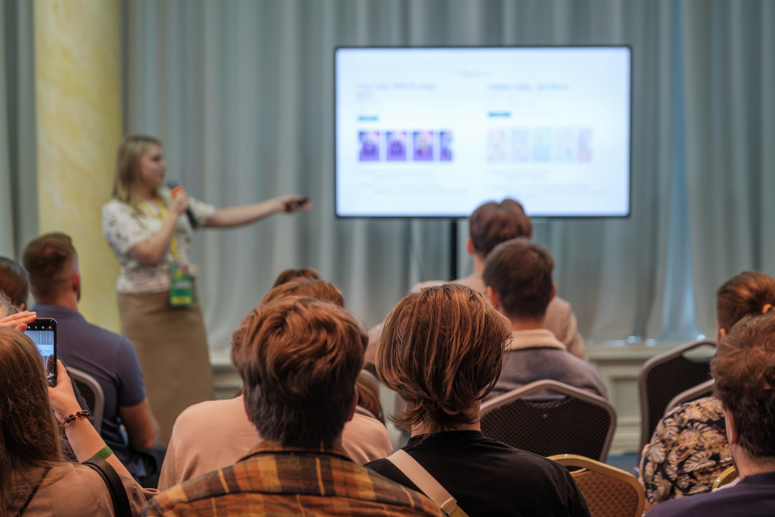 Audience watching a speaker pointing at a presentation slide on a large screen during a seminar.