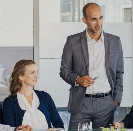 Man in business suit standing next to woman sitting at conference table