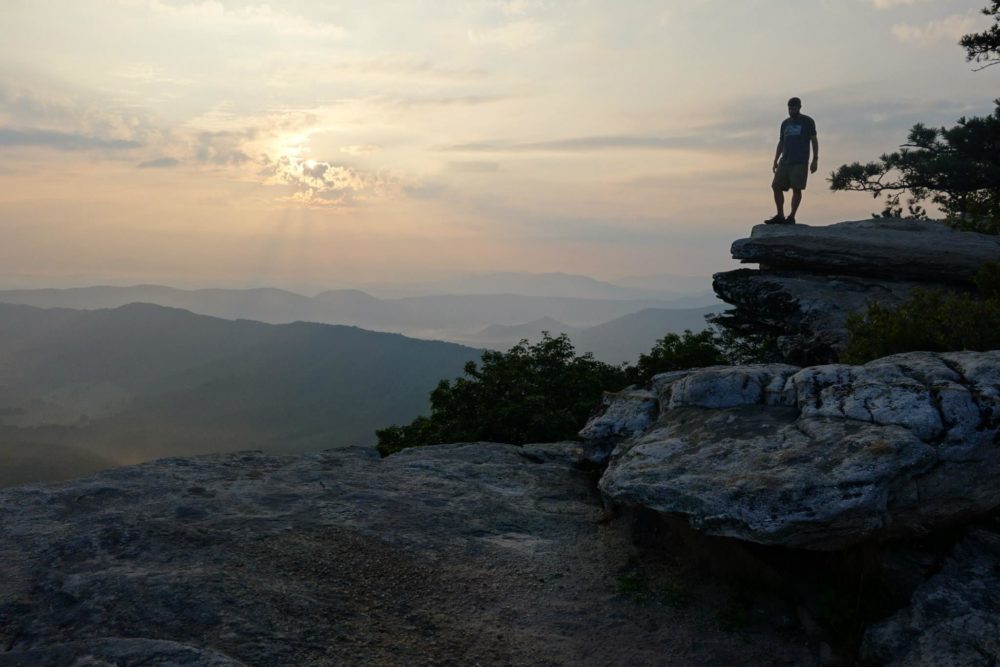 A Virginia Western hike participant stands on a mountaintop at sunrise