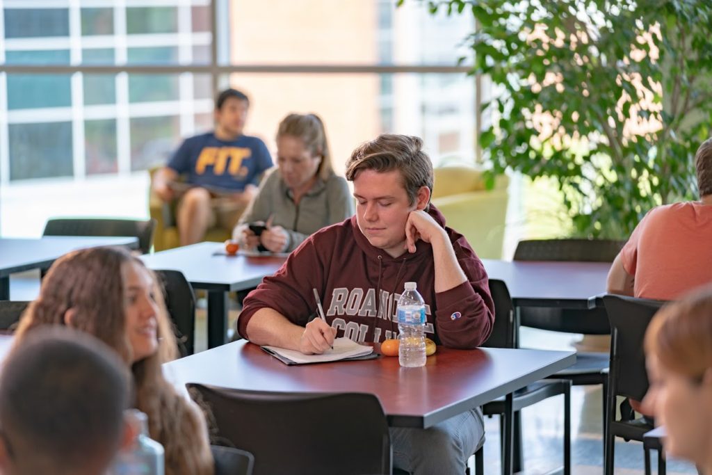 Students sitting in common area, focused on male student in Roanoke College sweatshirt